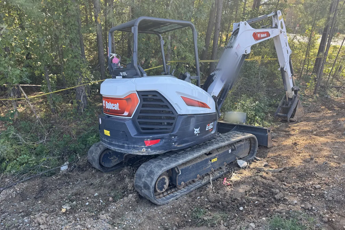 Compact excavator with a front blade at the edge of the woods