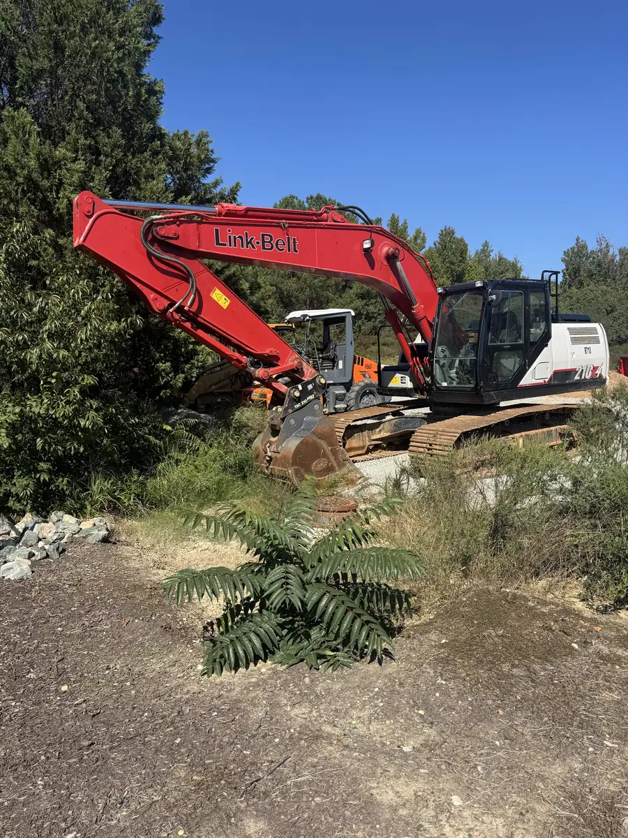 Full-size excavator parked beside brush at a site-work job