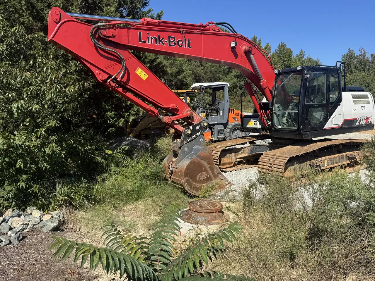 Full-size excavator at the wooded edge of a site-work job in the Richmond area