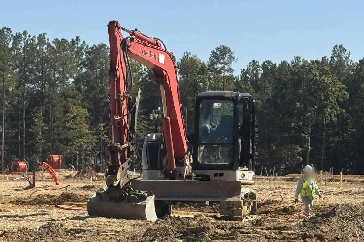 Mid-size excavator with a front blade on a cleared, graded site
