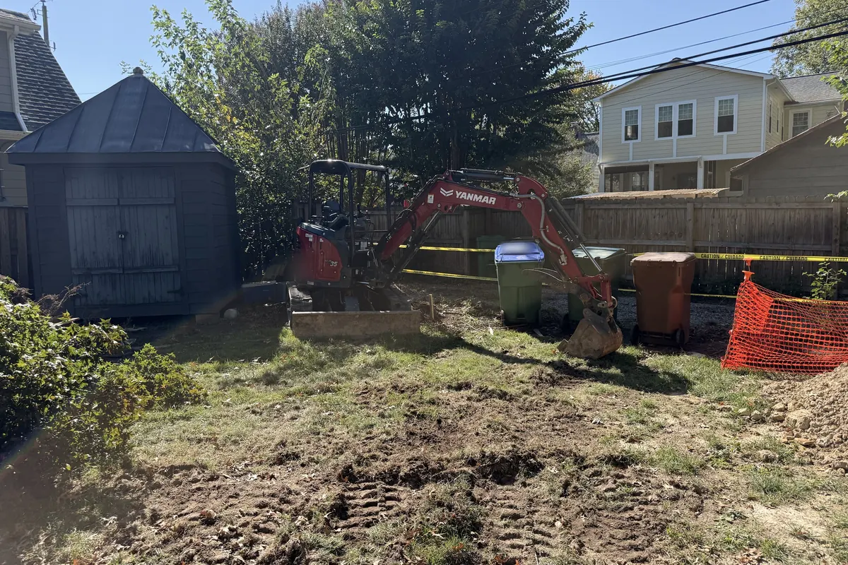 Mini excavator in a fenced backyard, with caution tape around the work area
